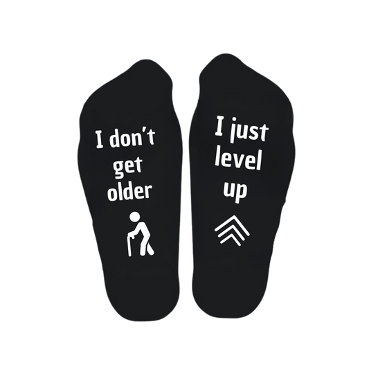 “Sokken met grappige tekst verdeeld over linker en rechter sok met de tekst "I don't get older / I just level up" – Handmade by J” verjaardag kado