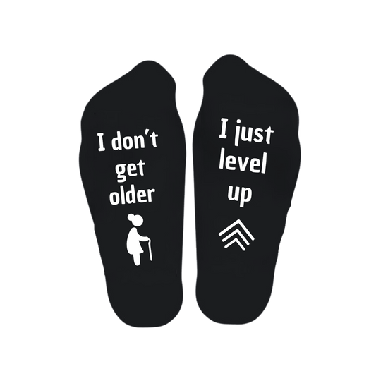 “Sokken met grappige tekst verdeeld over linker en rechter sok met de tekst "I don't get older / I just level up" – Handmade by J” verjaardag kado